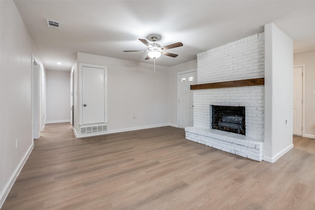 unfurnished living room with light wood-type flooring, a brick fireplace, visible vents, and baseboards