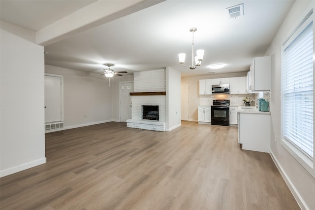 unfurnished living room with visible vents, a fireplace, light wood-style flooring, and ceiling fan with notable chandelier