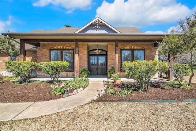 doorway to property with a porch, brick siding, and a shingled roof