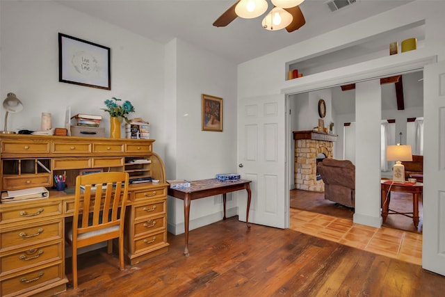 office space with ceiling fan, visible vents, a stone fireplace, and dark wood finished floors