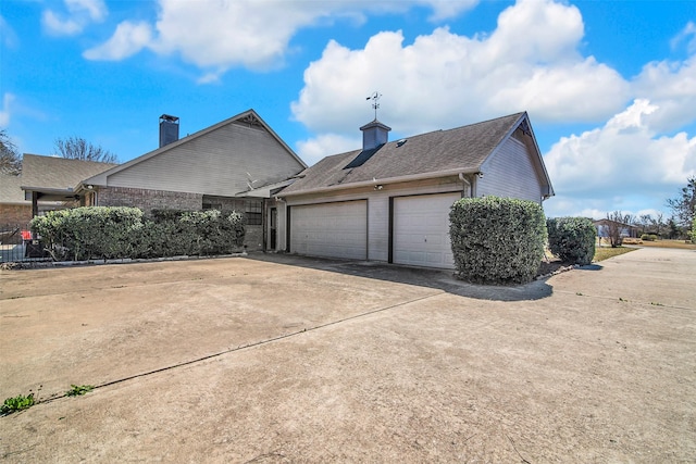 view of property exterior featuring brick siding, a chimney, concrete driveway, and a garage