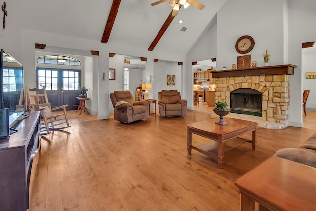 living area featuring ceiling fan, light wood-type flooring, beam ceiling, a fireplace, and high vaulted ceiling