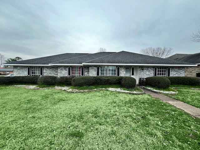 single story home with a shingled roof, a front yard, and brick siding