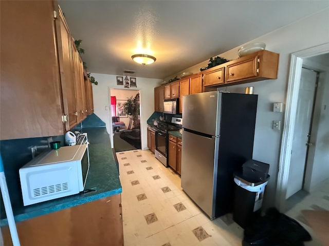 kitchen featuring black gas range, dark countertops, white microwave, brown cabinets, and freestanding refrigerator