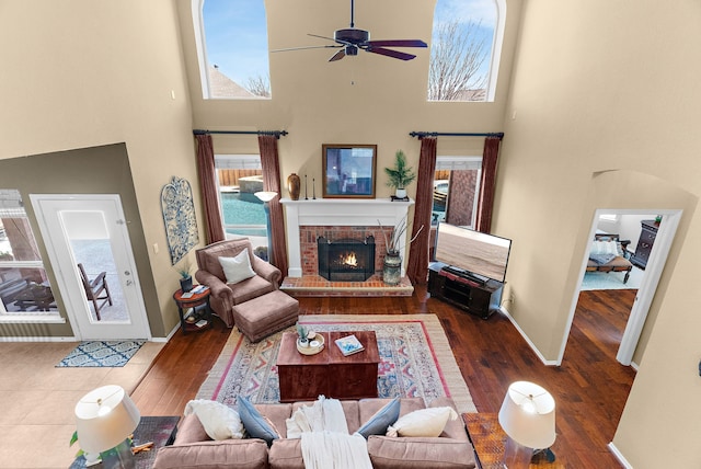 living area featuring a ceiling fan, wood finished floors, a high ceiling, a fireplace, and baseboards