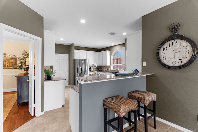 kitchen with visible vents, light stone counters, a peninsula, stainless steel refrigerator with ice dispenser, and white cabinets