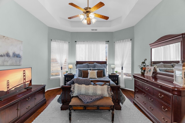 bedroom with visible vents, baseboards, a tray ceiling, and dark wood-style flooring