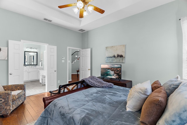 bedroom with visible vents, ensuite bathroom, a raised ceiling, and wood-type flooring