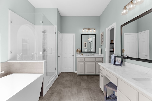 full bathroom with wood finished floors, a freestanding tub, two vanities, a stall shower, and a sink