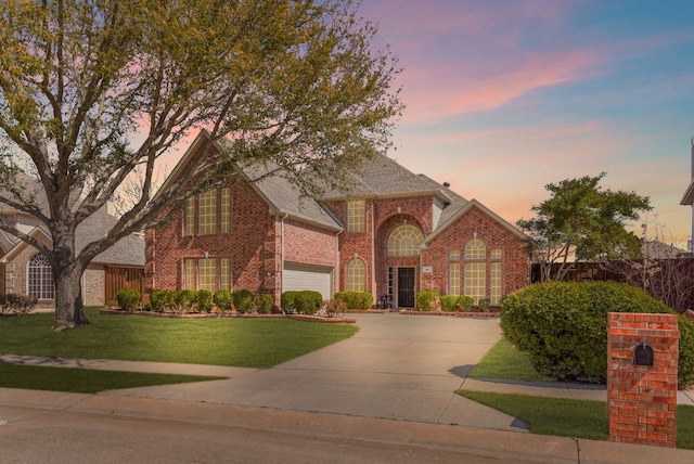 traditional home featuring a lawn, fence, concrete driveway, a garage, and brick siding