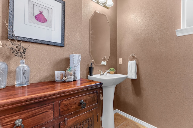 bathroom featuring tile patterned flooring, a textured wall, and baseboards