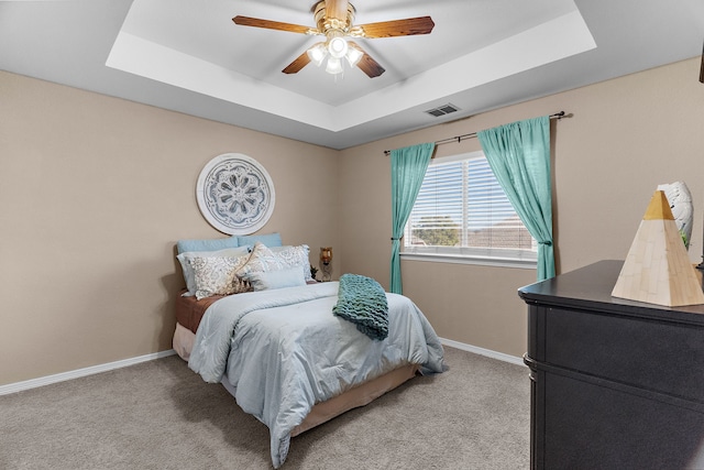 bedroom featuring a tray ceiling, baseboards, light colored carpet, and visible vents