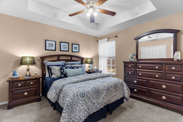 bedroom with light colored carpet, a tray ceiling, and ceiling fan