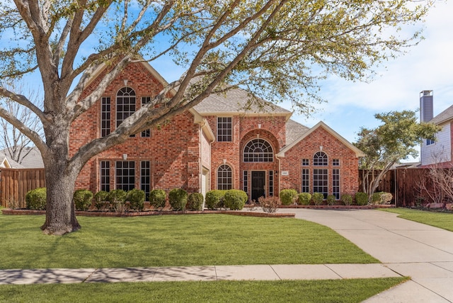 traditional-style house with driveway, brick siding, a front yard, and fence