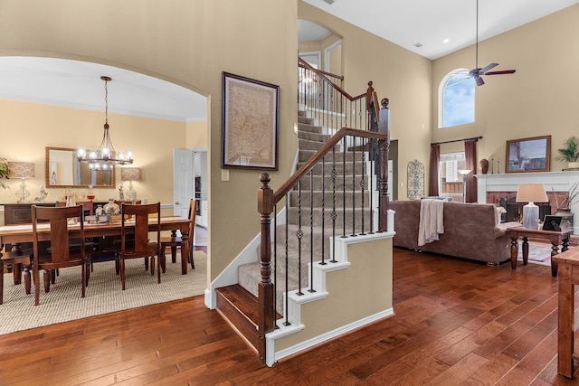 stairway with hardwood / wood-style floors, baseboards, arched walkways, a towering ceiling, and ceiling fan with notable chandelier