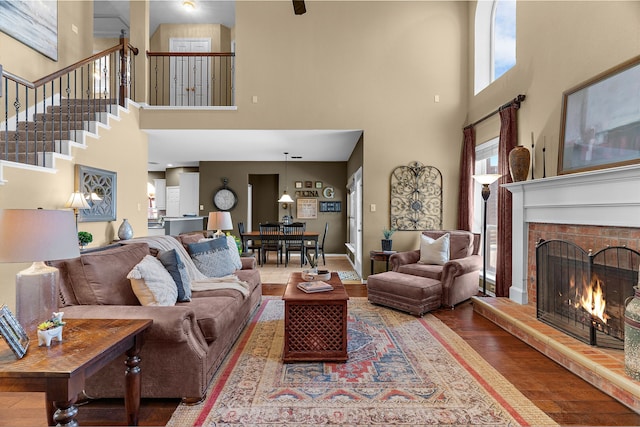 living area featuring stairway, a brick fireplace, baseboards, and wood finished floors