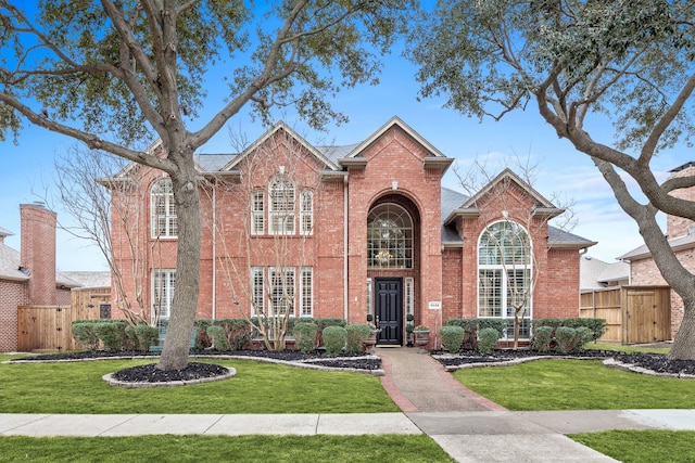 traditional home featuring brick siding, a front yard, and fence