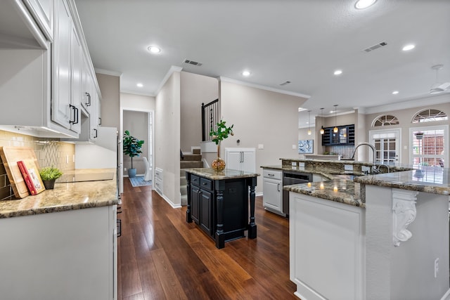 kitchen with a spacious island, white cabinetry, visible vents, and a sink