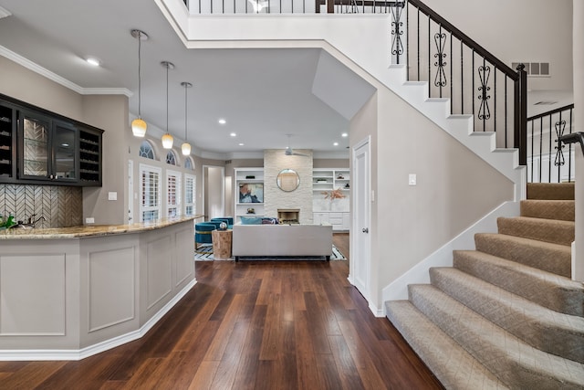 kitchen featuring visible vents, glass insert cabinets, dark wood-style flooring, light stone countertops, and crown molding