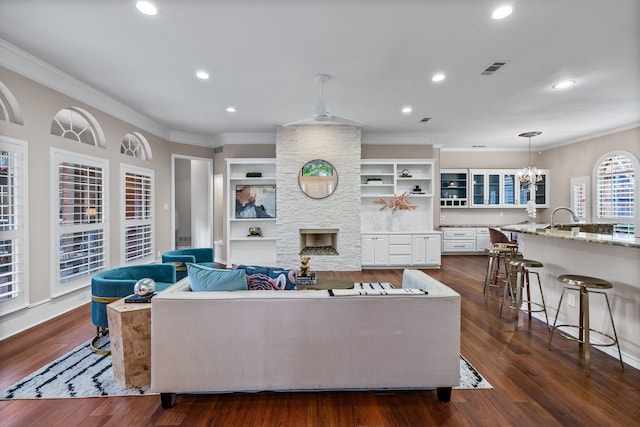 living area with a stone fireplace, ornamental molding, dark wood finished floors, and visible vents