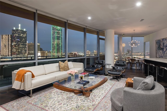 living room featuring a city view, a chandelier, visible vents, wood finished floors, and a wall of windows