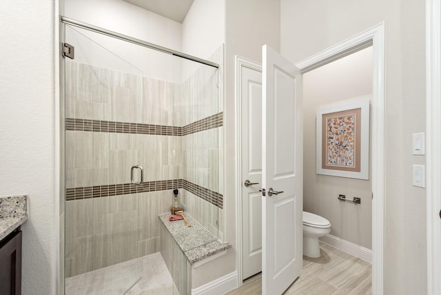 bathroom with vanity, a shower stall, toilet, and baseboards