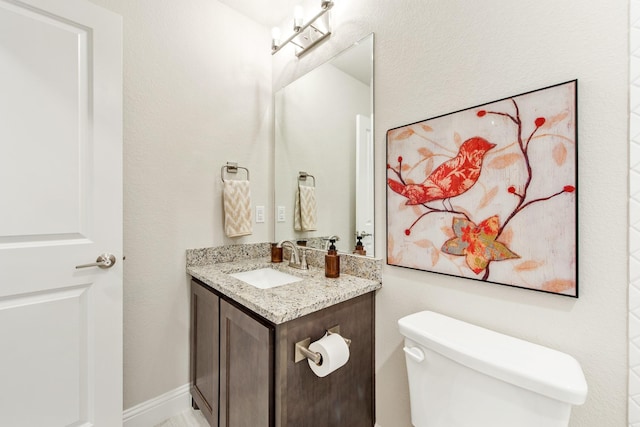 half bathroom featuring toilet, baseboards, and vanity