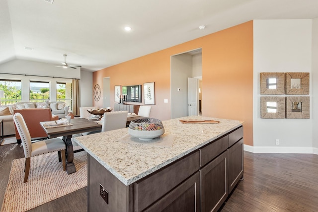 kitchen featuring dark wood-type flooring, a center island, dark brown cabinetry, and light stone countertops