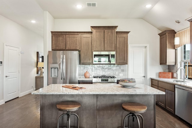 kitchen featuring a center island, stainless steel appliances, visible vents, vaulted ceiling, and a sink