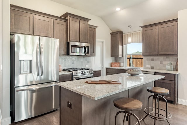 kitchen with appliances with stainless steel finishes, a center island, light stone countertops, vaulted ceiling, and a sink