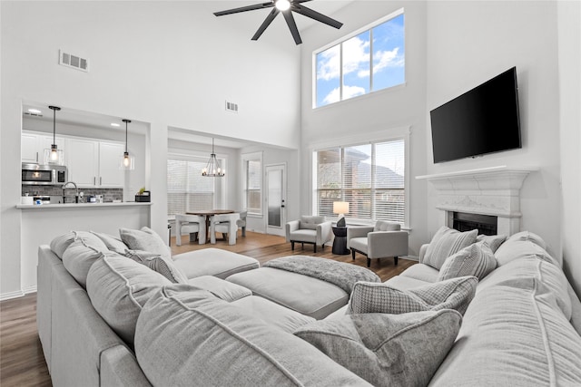 living area with a premium fireplace, visible vents, ceiling fan with notable chandelier, and wood finished floors