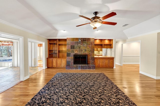 living area featuring built in shelves, light wood finished floors, a tiled fireplace, ornamental molding, and baseboards