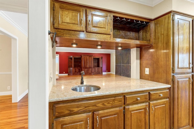 kitchen featuring brown cabinets, crown molding, a sink, light stone countertops, and light wood-type flooring