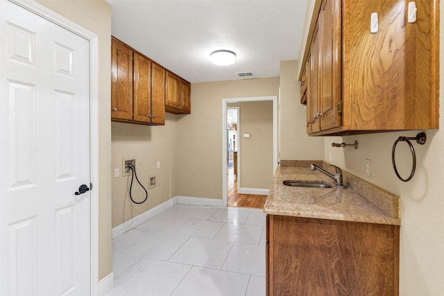 kitchen with baseboards, a sink, light stone countertops, and brown cabinets