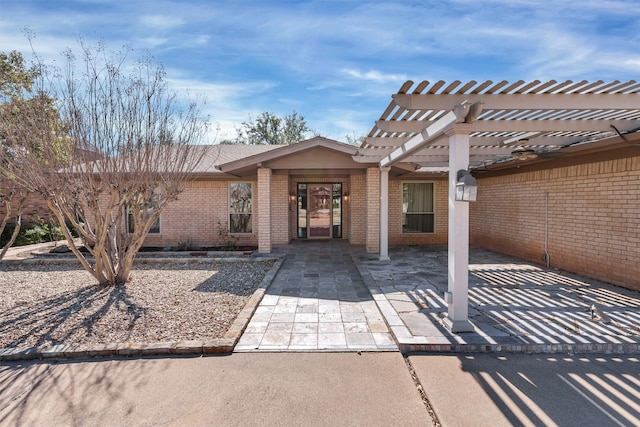 property entrance featuring brick siding, a patio, and a pergola