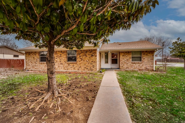 view of front of house featuring a shingled roof, brick siding, fence, and a front lawn