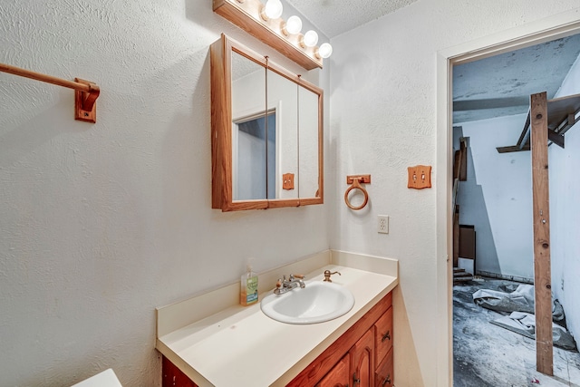 bathroom with a textured ceiling, a textured wall, unfinished concrete flooring, and vanity