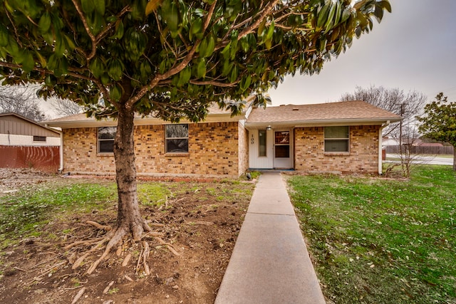 ranch-style house with a shingled roof, a front yard, brick siding, and fence