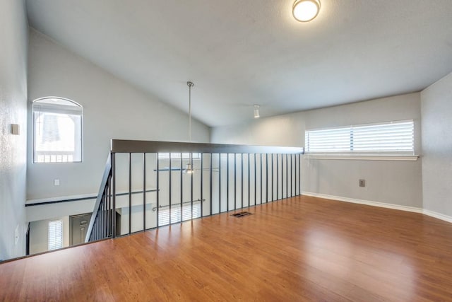 unfurnished room featuring lofted ceiling, baseboards, visible vents, and wood finished floors