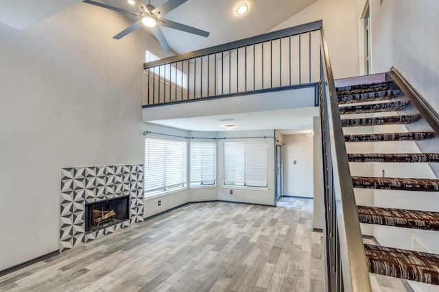 interior space with a fireplace, a ceiling fan, wood finished floors, high vaulted ceiling, and baseboards