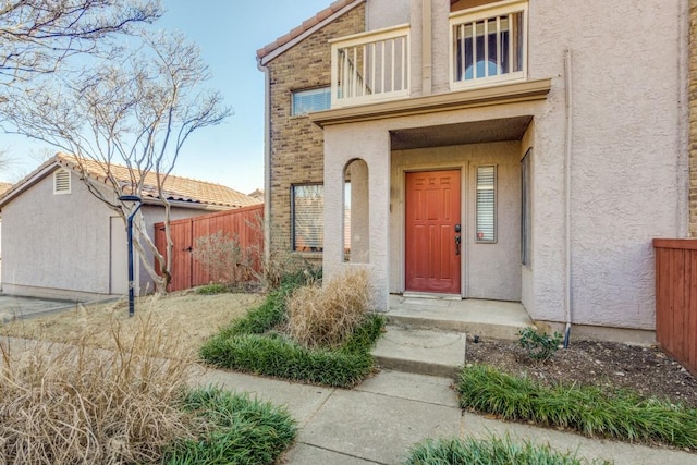 view of exterior entry with a balcony, fence, and stucco siding