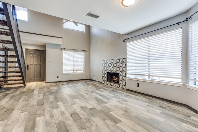 unfurnished living room with light wood-style flooring, a stone fireplace, visible vents, and stairway