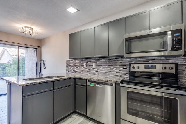 kitchen featuring backsplash, gray cabinetry, appliances with stainless steel finishes, a sink, and a peninsula