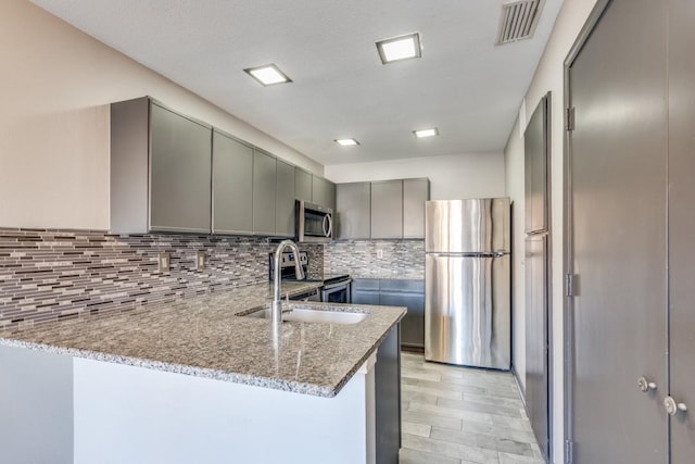 kitchen with light stone counters, gray cabinetry, stainless steel appliances, visible vents, and tasteful backsplash