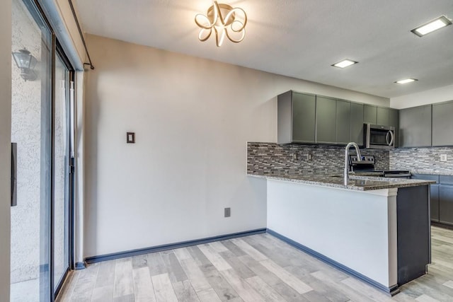 kitchen with backsplash, gray cabinetry, appliances with stainless steel finishes, stone countertops, and a peninsula