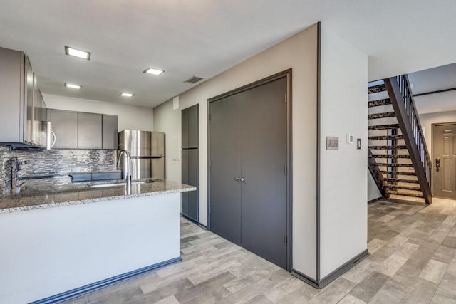 kitchen with gray cabinetry, freestanding refrigerator, light stone countertops, range, and a peninsula