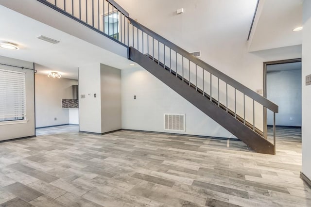 unfurnished living room with a towering ceiling, stairway, wood finished floors, and visible vents