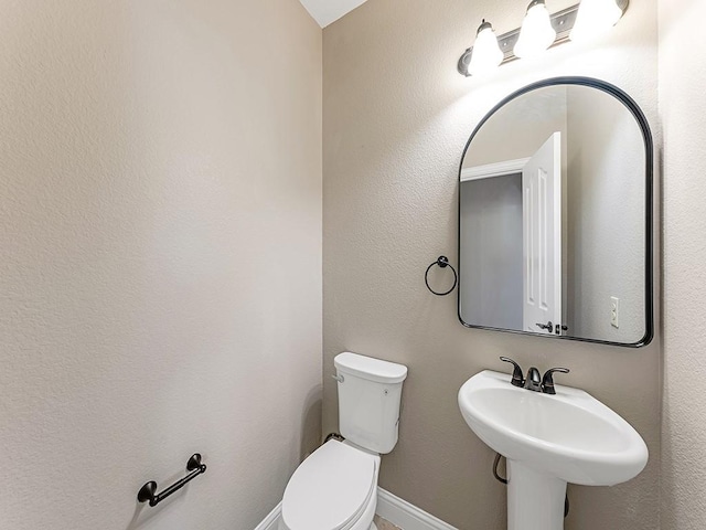 half bath featuring toilet, baseboards, and a sink