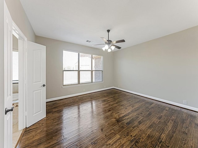 empty room featuring a ceiling fan, visible vents, baseboards, and wood finished floors