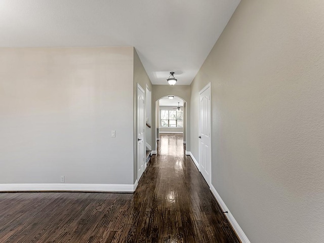 corridor featuring arched walkways, dark wood-style floors, and baseboards